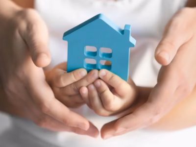Manos de adulto y niño sosteniendo una casa azul, representando la protección del menor en custodia y alimentos.
