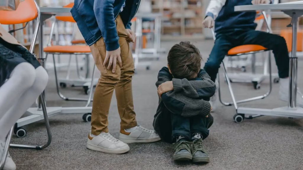 Escolar sentado en el suelo del aula sufriendo bullying, ilustrando el protocolo legal contra el acoso escolar
