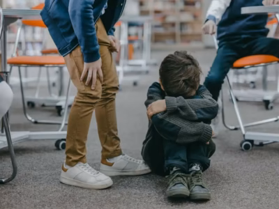 Escolar sentado en el suelo del aula sufriendo bullying, ilustrando el protocolo legal contra el acoso escolar