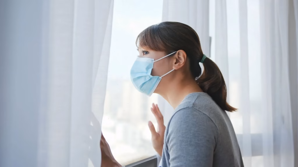 Mujer con mascarilla mirando por la ventana durante el confinamiento por sanciones del estado de alarma.