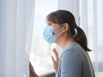 Woman wearing a mask looking through a window during the lockdown regarding state of alarm sanctions.