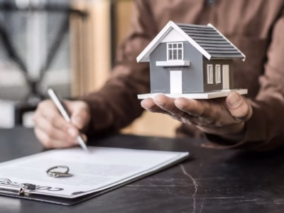 Persona firmando documentos con alianzas y una casa para ilustrar la proteccion del patrimonio en procesos de divorcio y estabilidad.