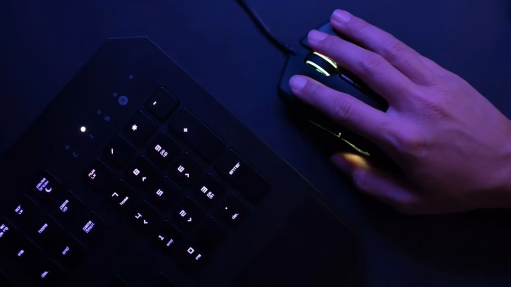 Mano utilizando un ratón y teclado gaming en entorno oscuro, simbolizando el origen de un ciberataque de smishing.