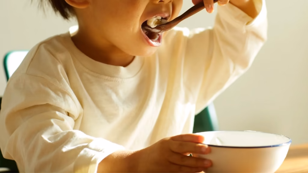 Niño pequeño comiendo de un cuenco con una cuchara. Cálculo de pensión alimenticia.