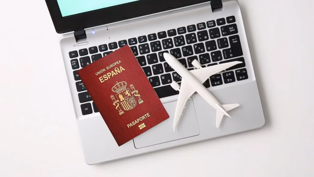 Pasaporte español y maqueta de avión sobre un ordenador portátil para tramitar visados de residencia y trabajo.
