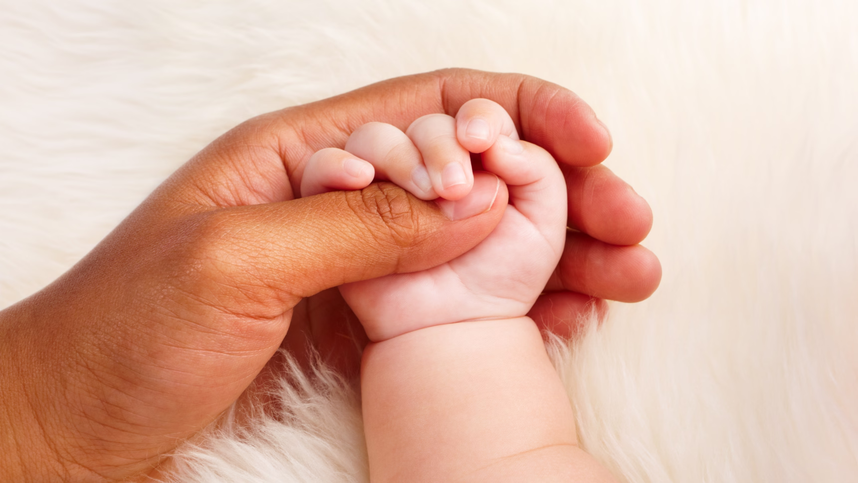 Mano de un adulto sujetando la mano de un bebé como representación de la adopción internacional y la creación de nuevos vínculos familiares.
