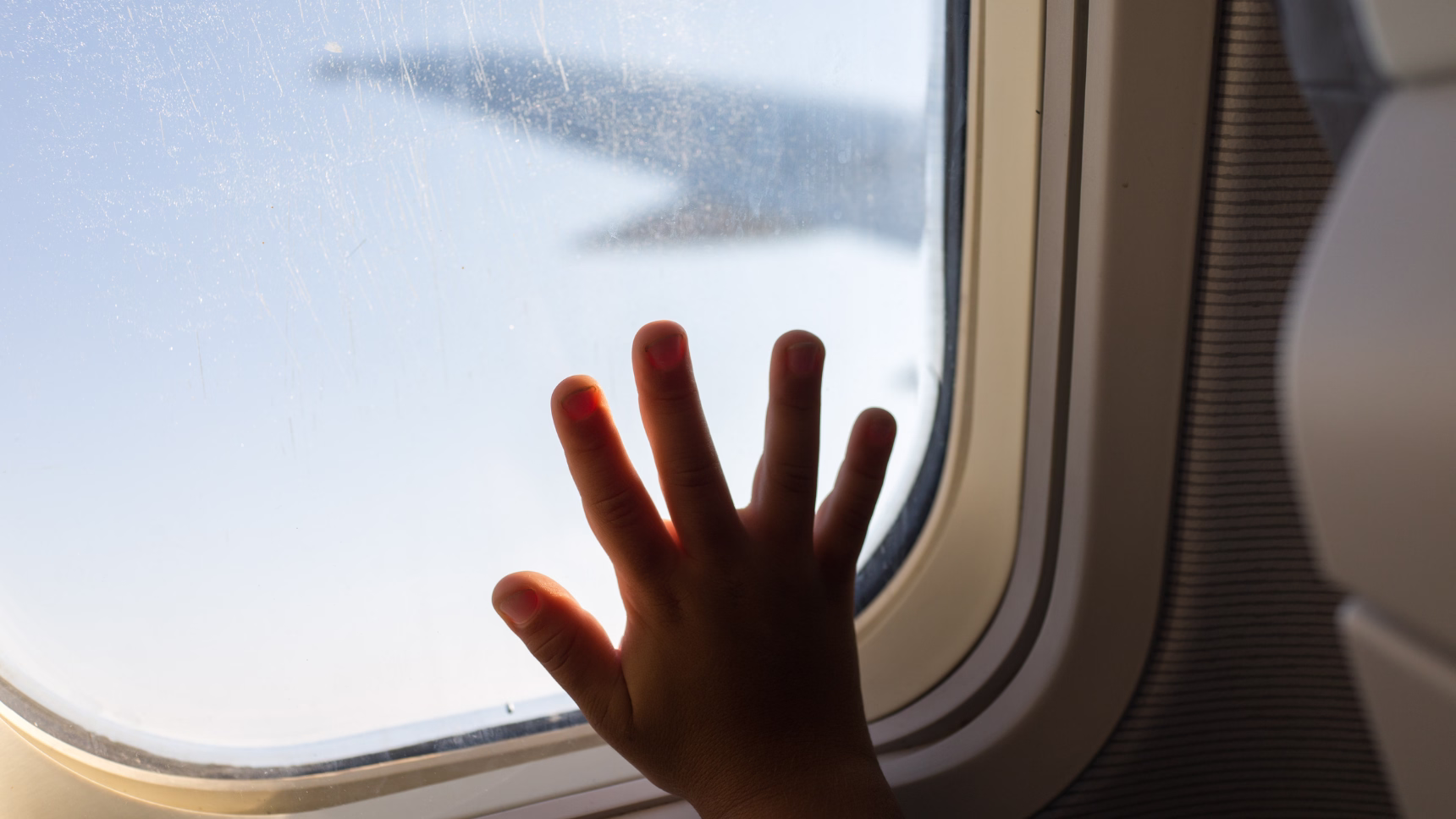 Mano de un menor junto a la ventanilla de un avión como representación de la sustracción internacional de menores.
