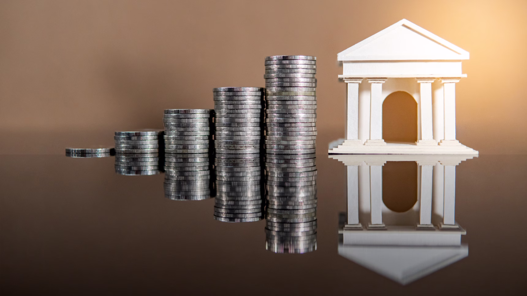 Maqueta de un banco junto a monedas apiladas que representan las cuentas bancarias en España de un extranjero fallecido.