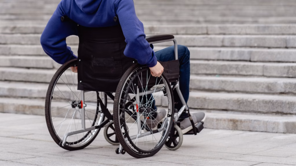Persona en silla de ruedas frente a unas escaleras, imagen ilustrativa de las limitaciones físicas relacionadas con la incapacidad permanente.
