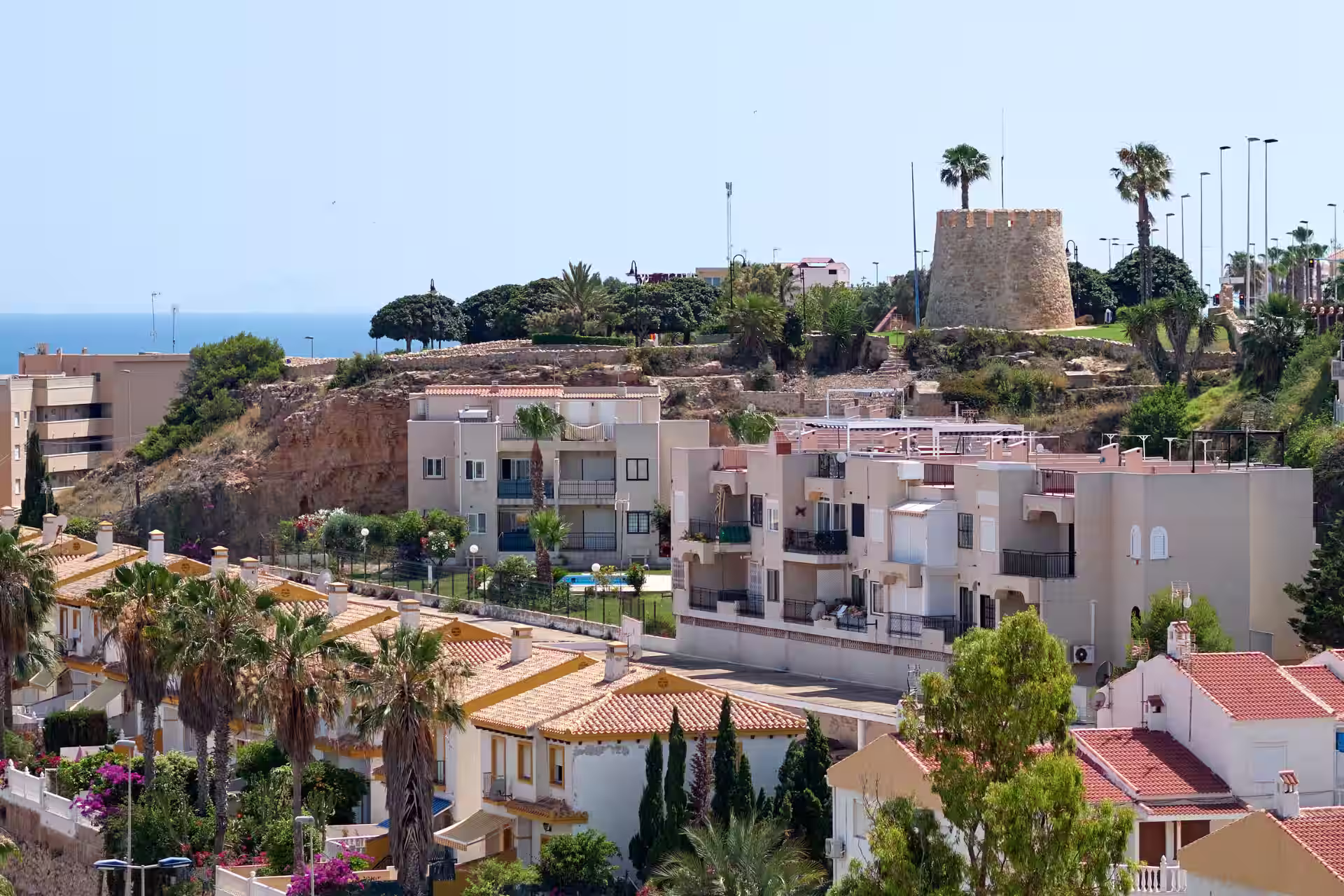 Torre del Moro de Torrevieja sobre una elevación junto a viviendas y vegetación mediterránea.