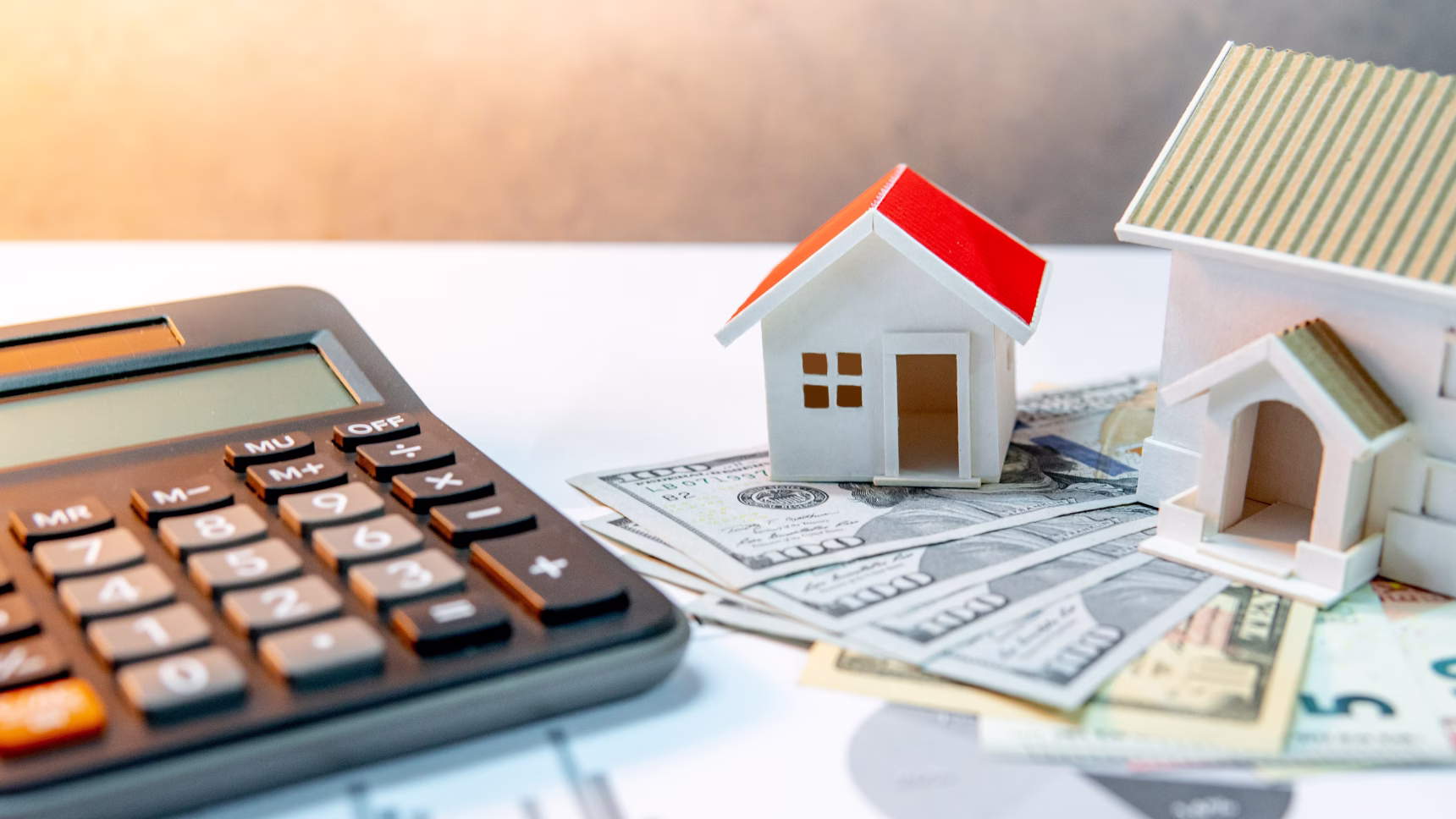 Calculadora, dinero y maquetas de viviendas que ilustran la venta de una vivienda heredada en España desde el extranjero.