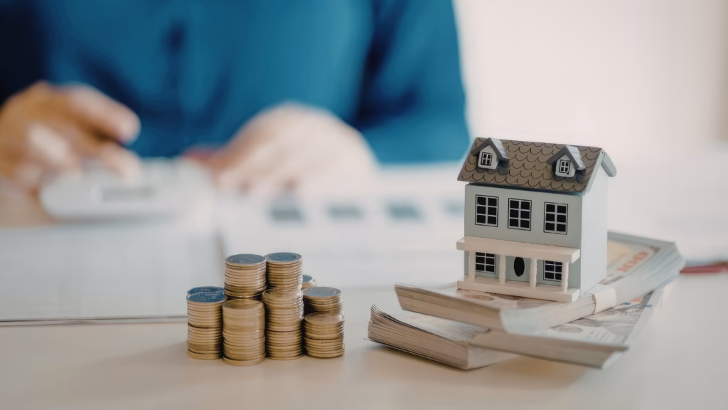 Venta de una VPO: maqueta de vivienda sobre billetes y monedas que representan el precio máximo legal de una vivienda protegida.